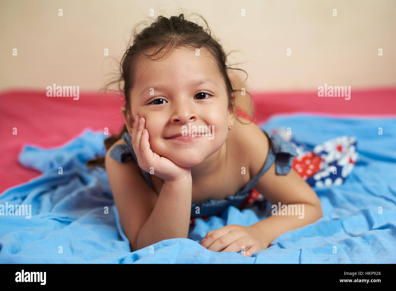 smiling latino girl laying on blue blanket bed Stock Photo