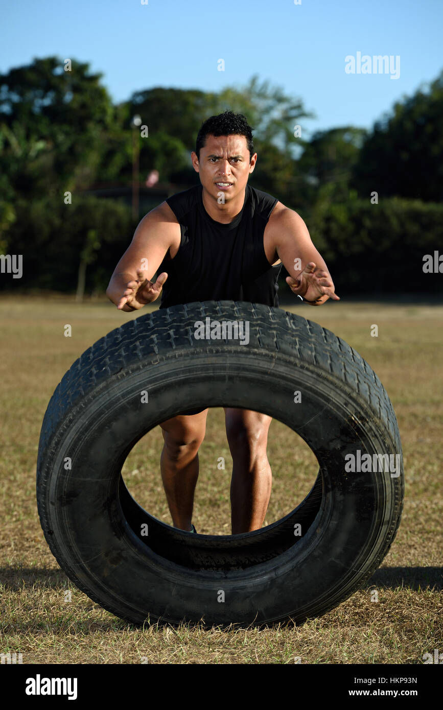 sportman flipping huge tire on grass stadium Stock Photo