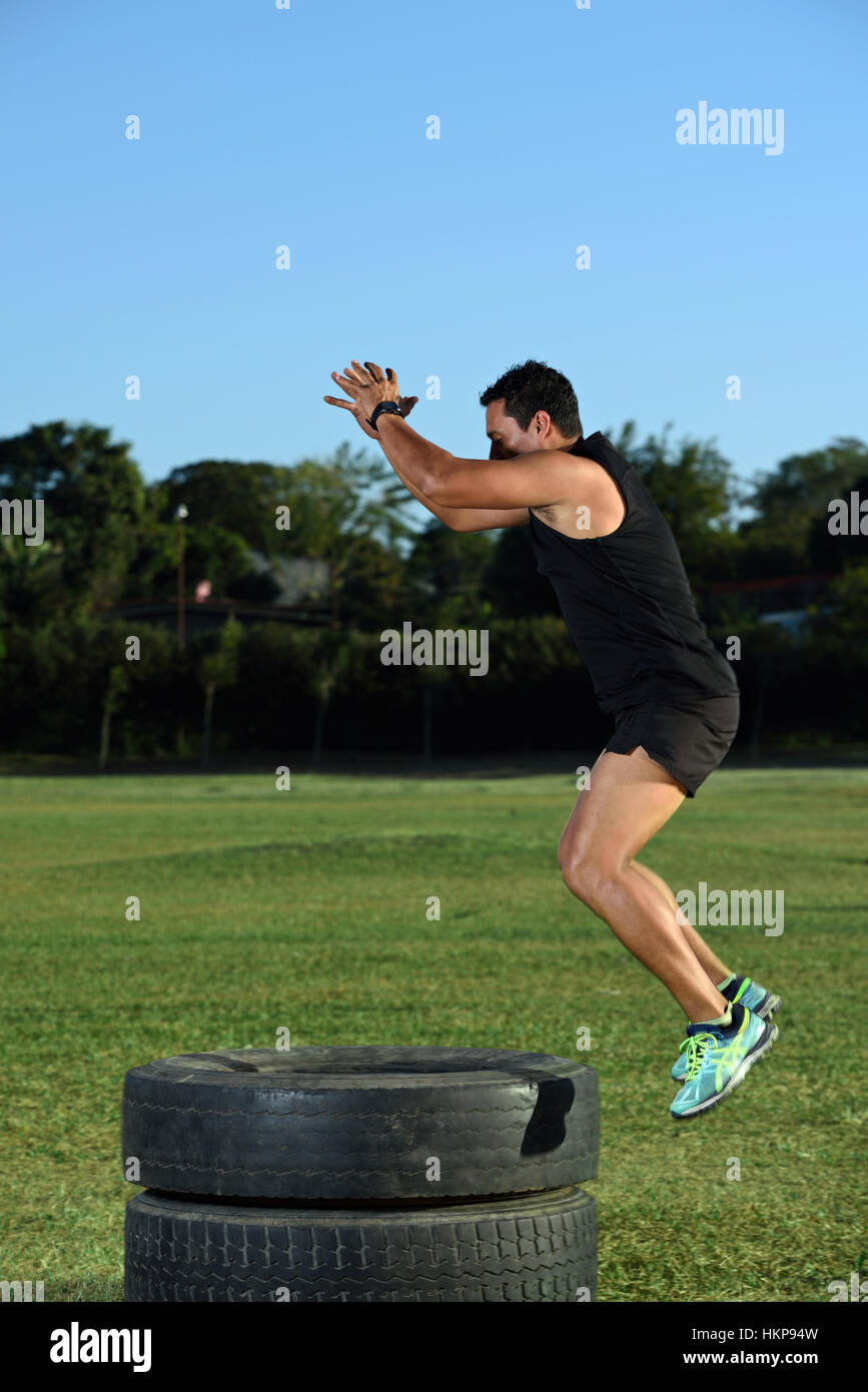 workout man jump in air on tire on green grass Stock Photo