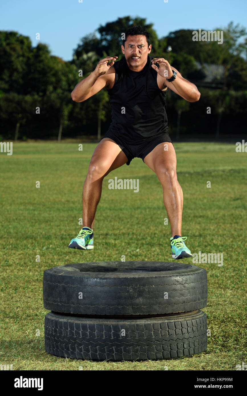 sportman jump on tire in green grass park Stock Photo