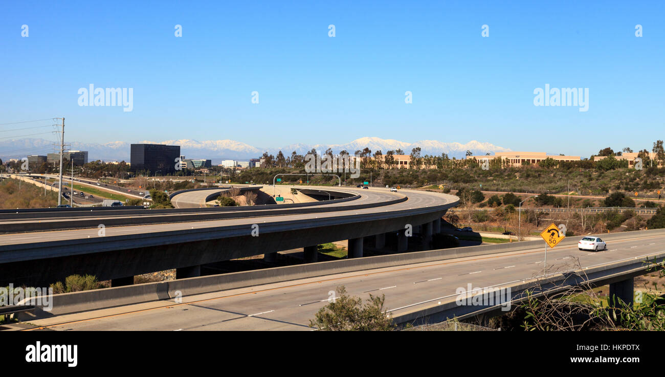 Highway exit headed from Newport Beach into Irvine, California, USA, with white-capped mountains in the distance and a blue sky Stock Photo