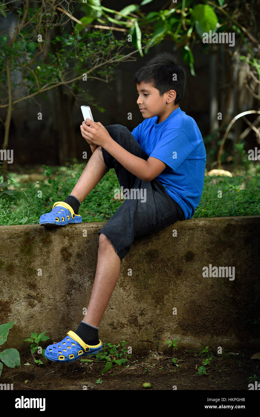 kid with phone sit in concrete green garden Stock Photo