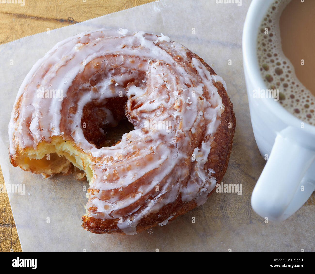 Glazed cruller donut on wax paper next to a mug of hot coffee Stock Photo