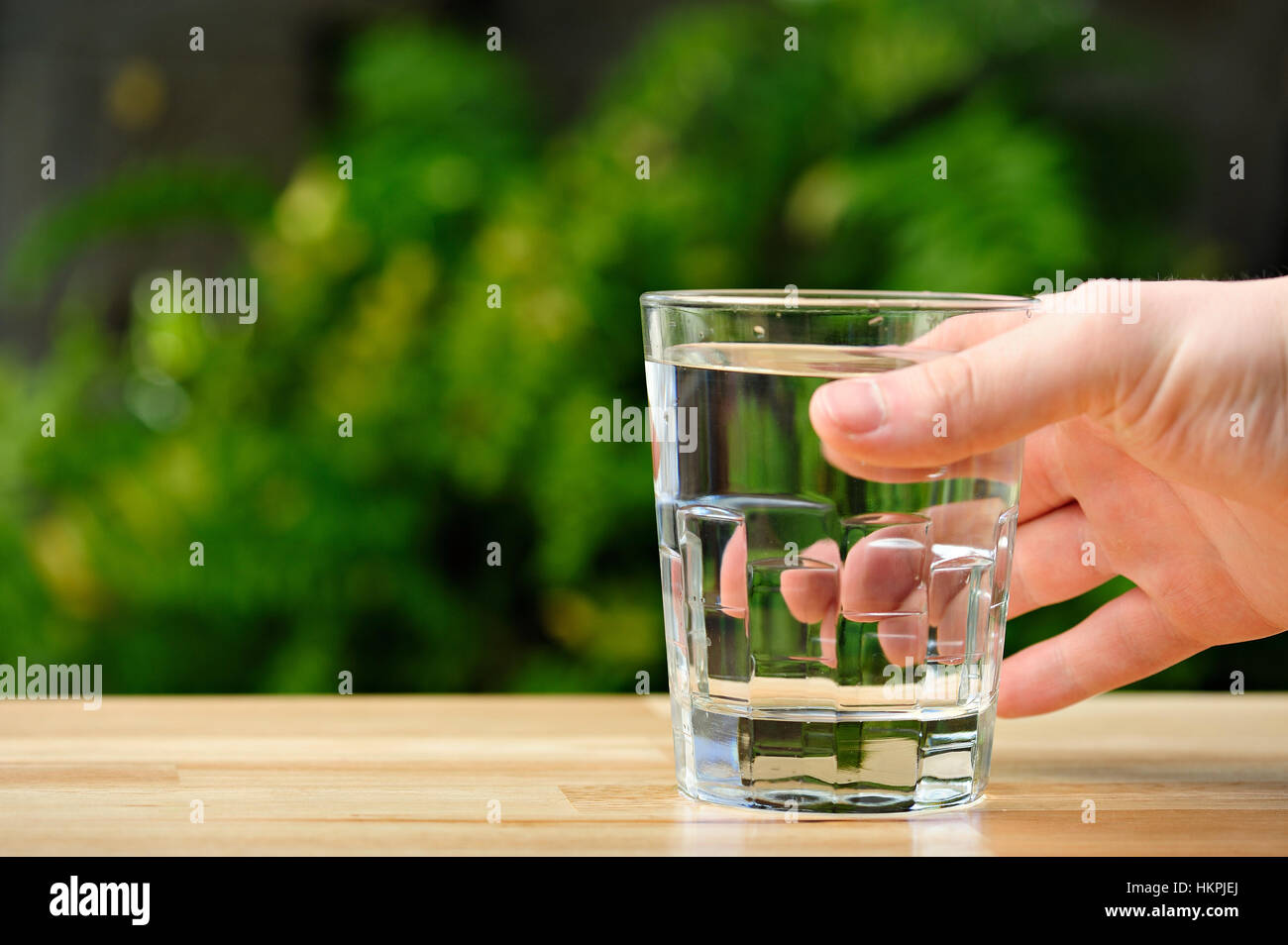 glass of water in hand on table in green park background Stock Photo