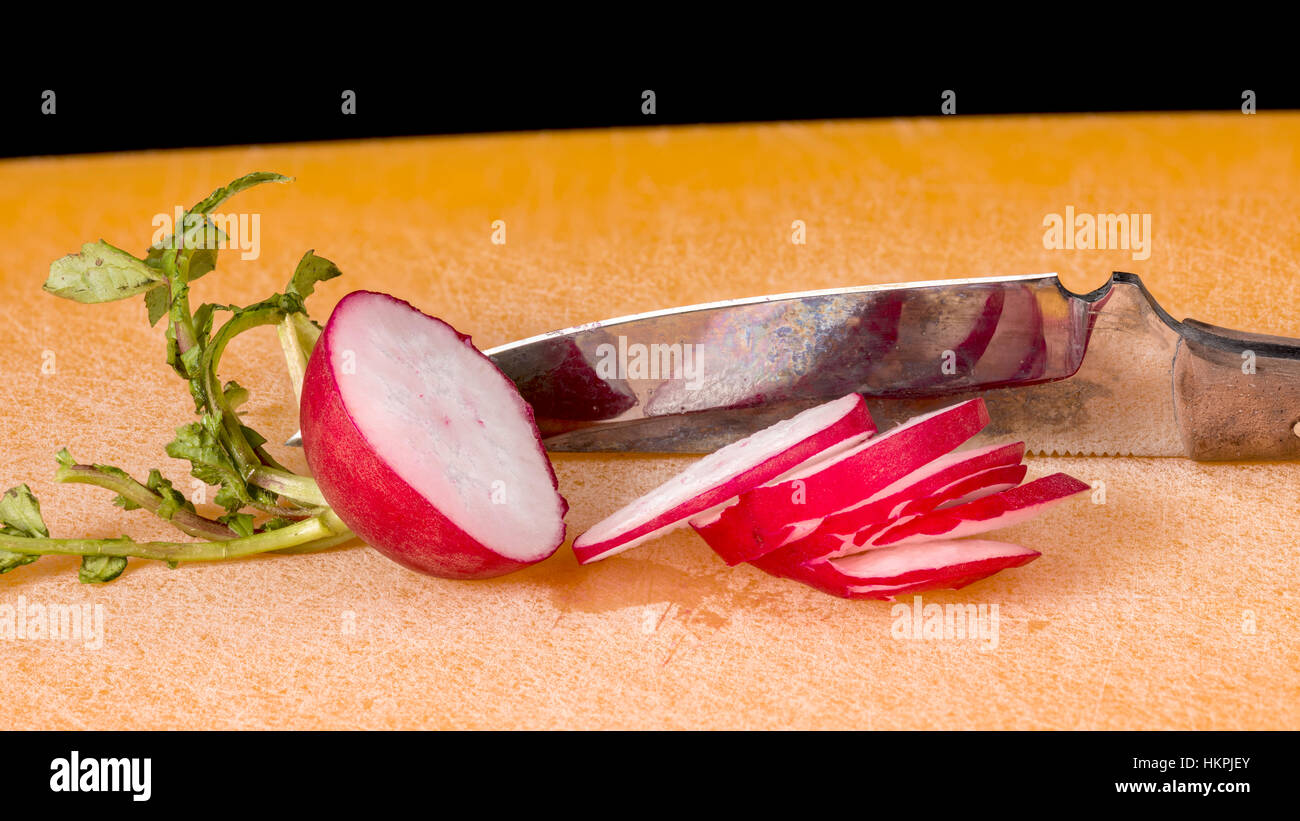 Fresh radish that has been sliced on a cutting board that is orange Stock Photo