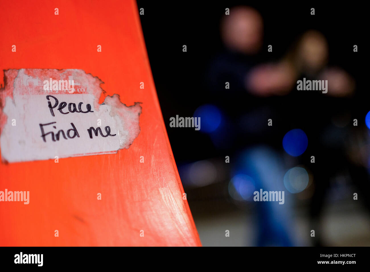 'Peace find me' sticker attached to the orange colour bench on Bankside; people passing in motion. Stock Photo