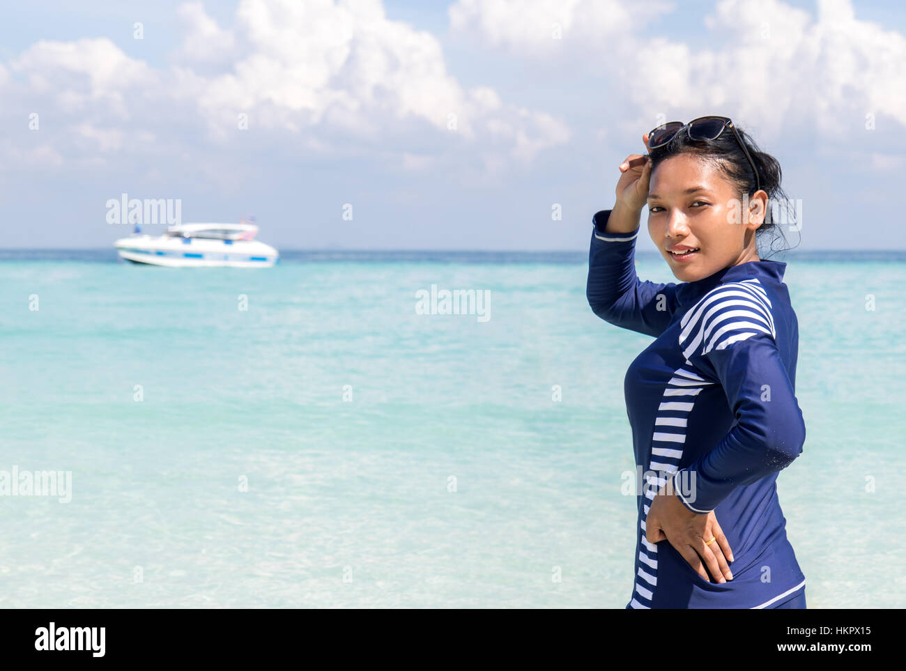 Woman in a full-body swimsuit stands on sea beach, at background