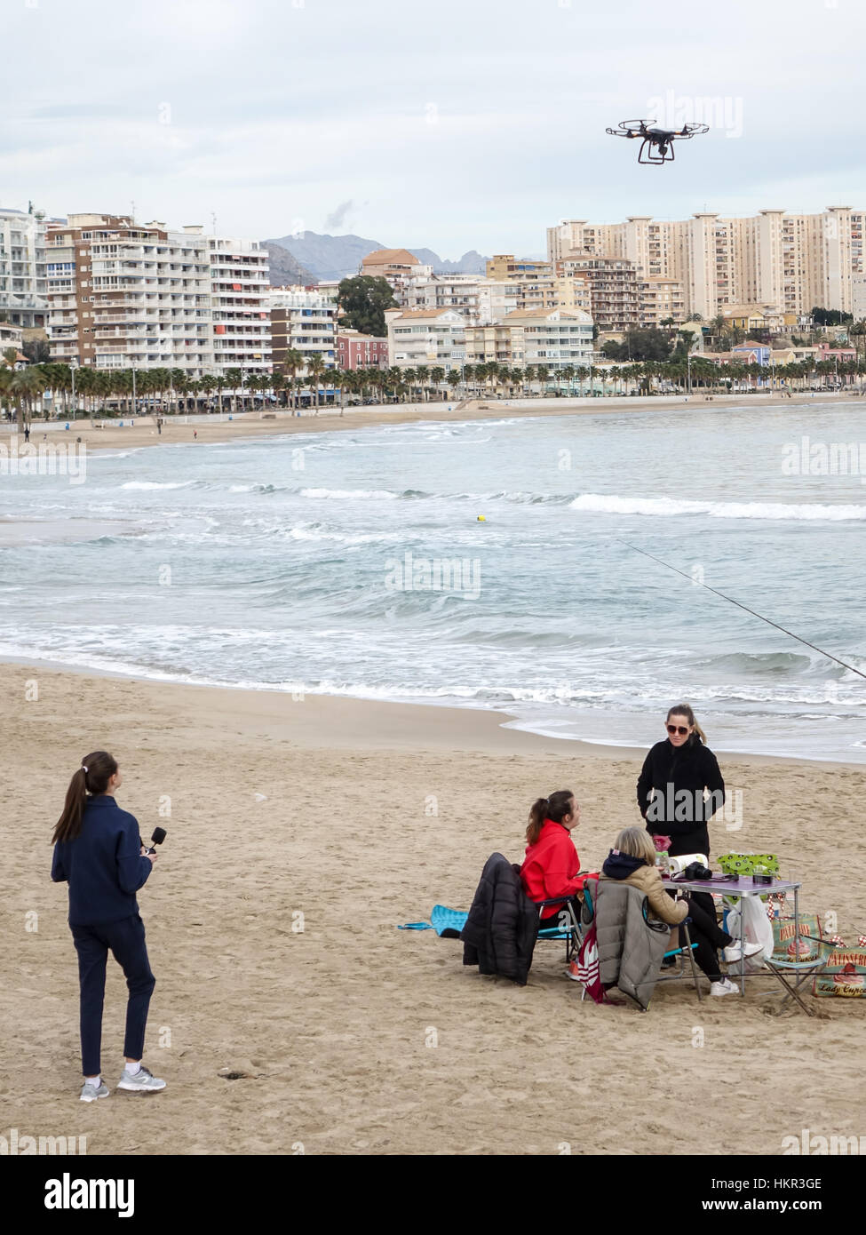 Family fishing on a beach in Villajoyosa, Alicante Province, Spain. Young girl flies quadcopter drone. Stock Photo