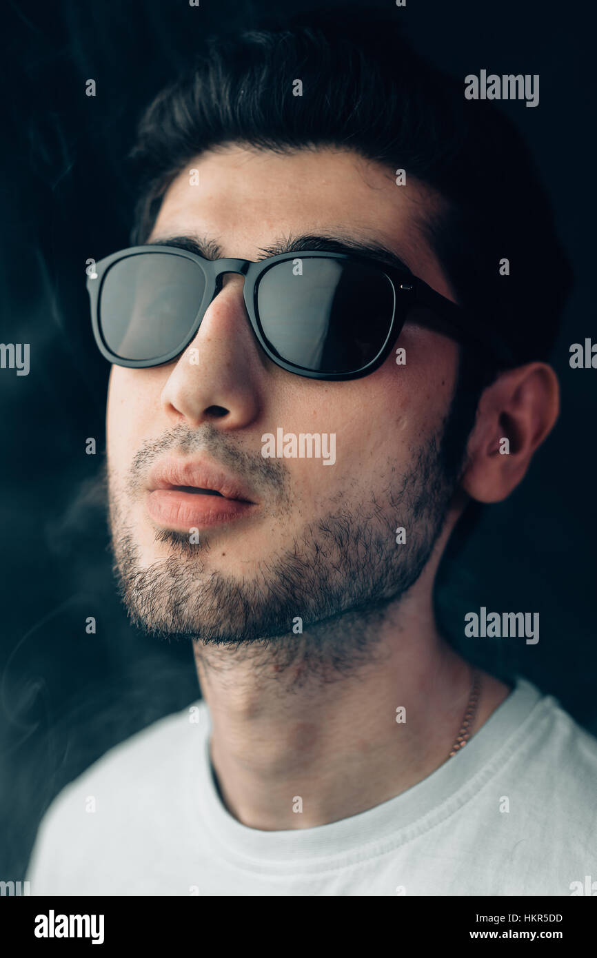Armenian stylish guy in sun glasses on a smoky background. Vertical studio portrait in close-up. Stock Photo