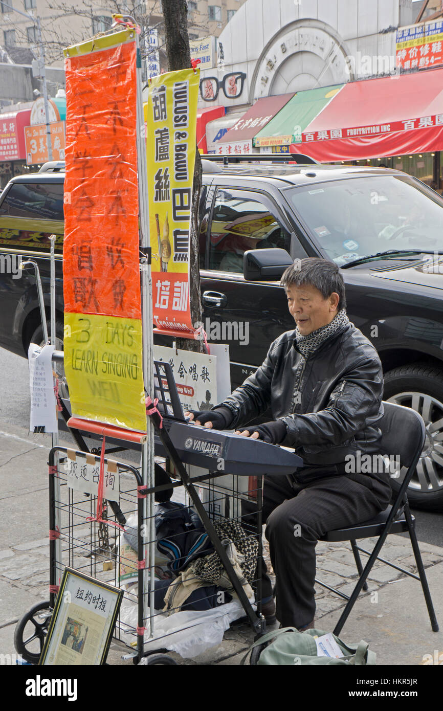 A Korean man playing the piano on Main Street on a winter afternoon in Flushing advertising singing lessons Stock Photo