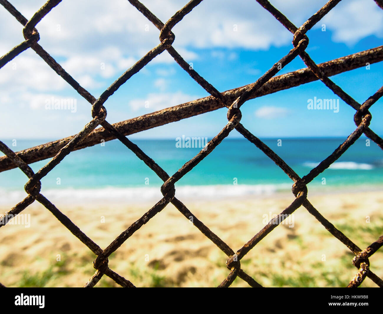 Closeup photo of a rusty old chain link fence with a beach in the