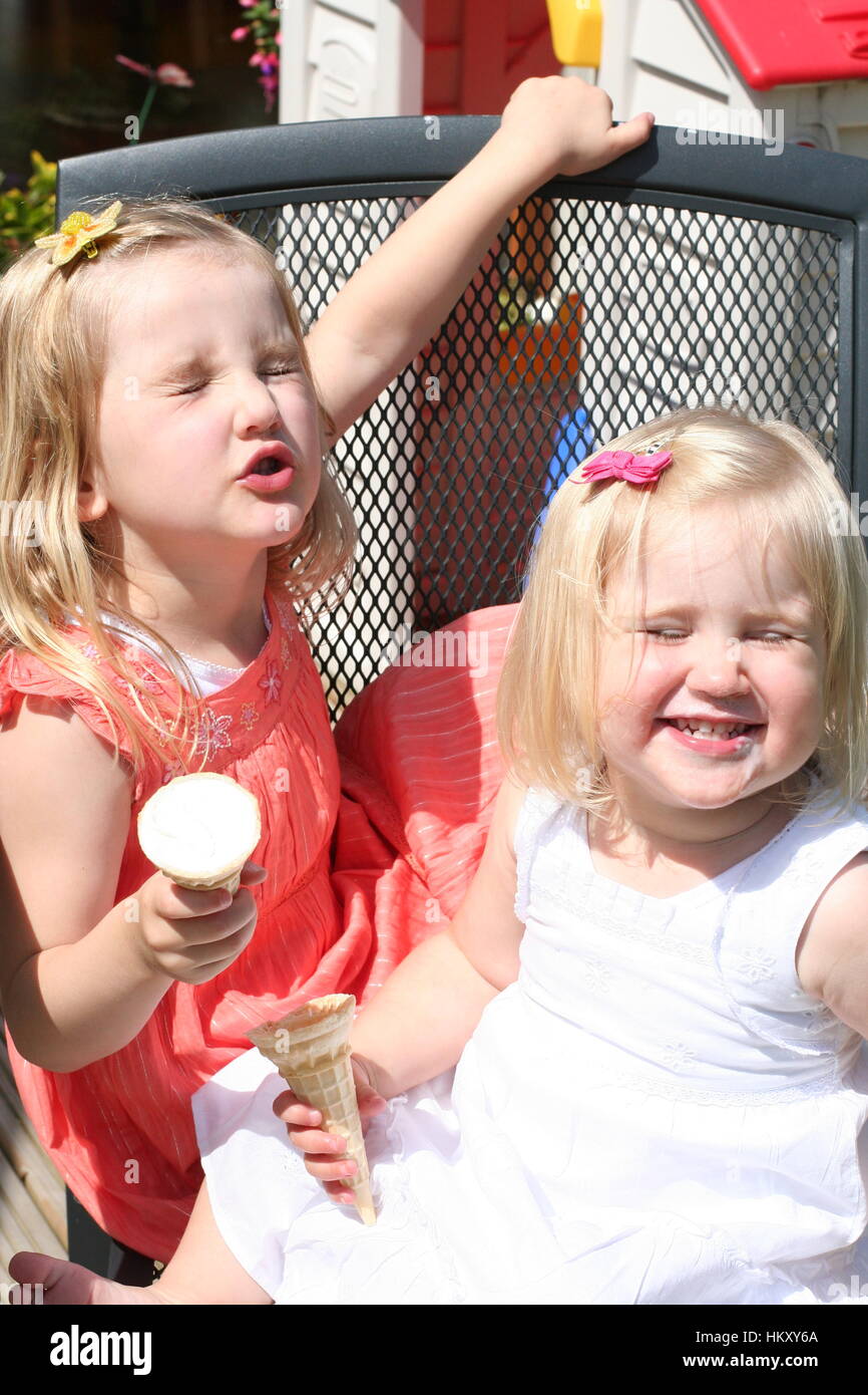 Two blonde Little girls, children kids laughing  messing making faces eating icecream cones garden best life, giddy happy concept, joy bliss fun sun Stock Photo