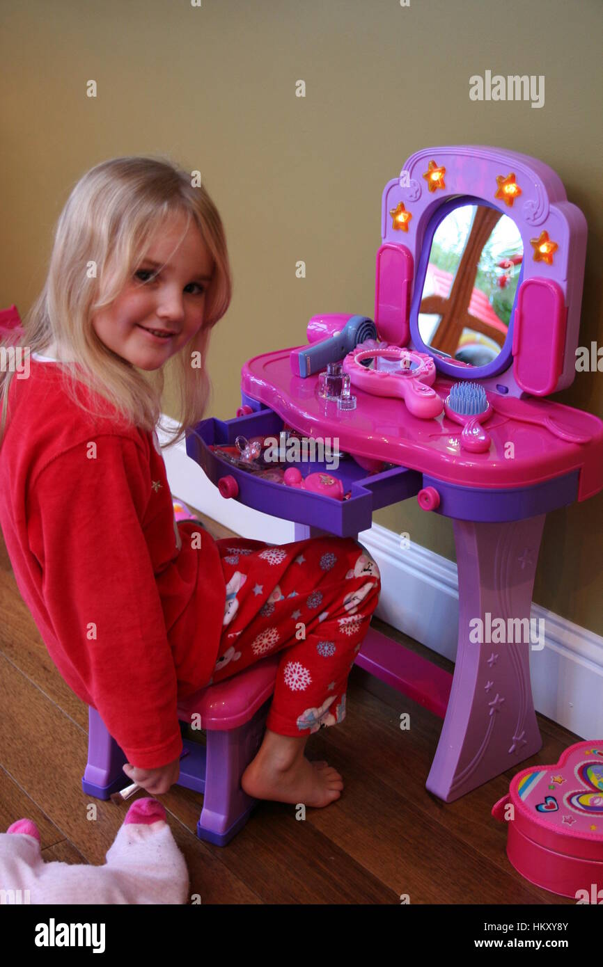 Little blonde girl child kid trying out her new makeup at her makeup table on christmas morning concept, wearing eyeshadow, a gift from Santa Stock Photo