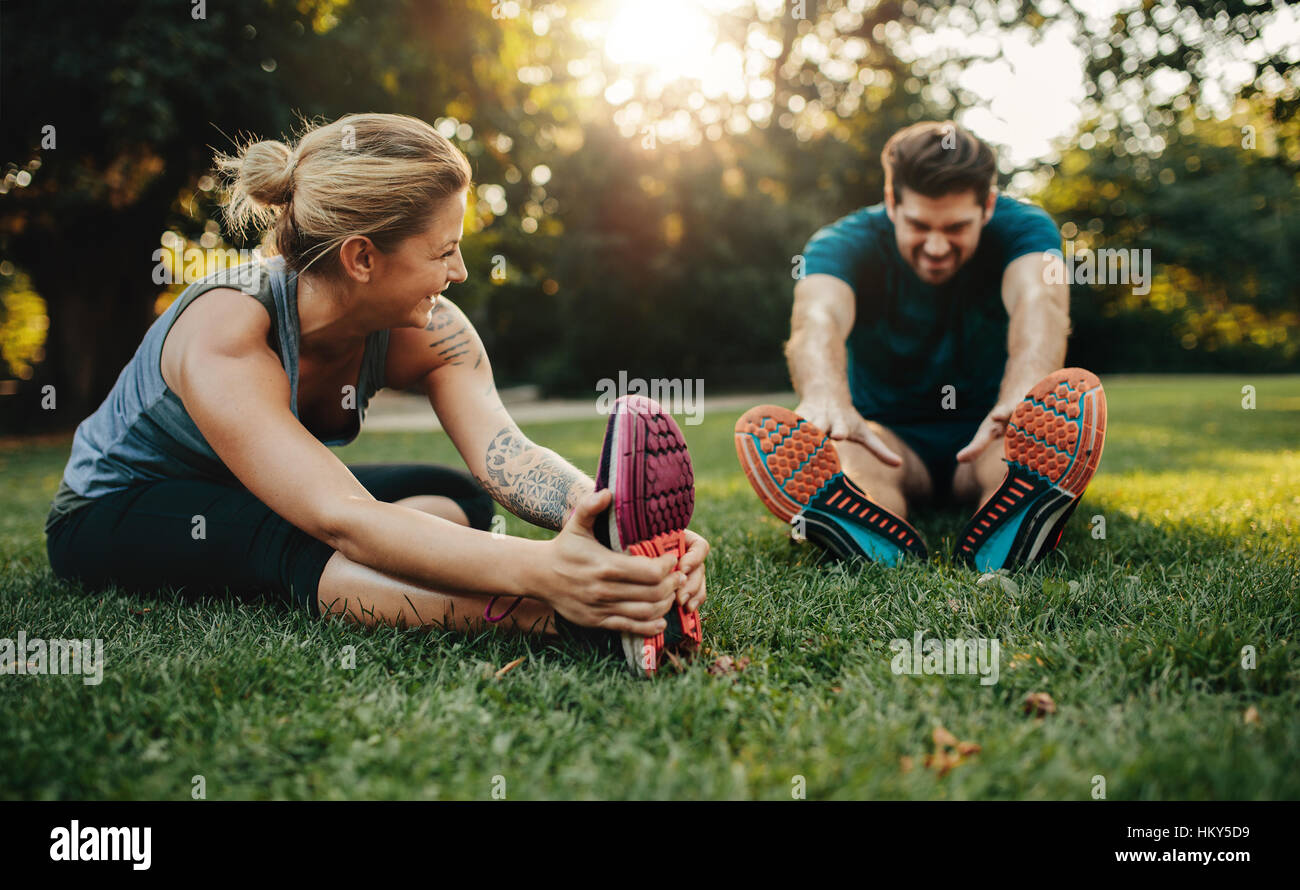 Happy young man and woman stretching in the park. Smiling caucasian couple exercising in morning. Stock Photo