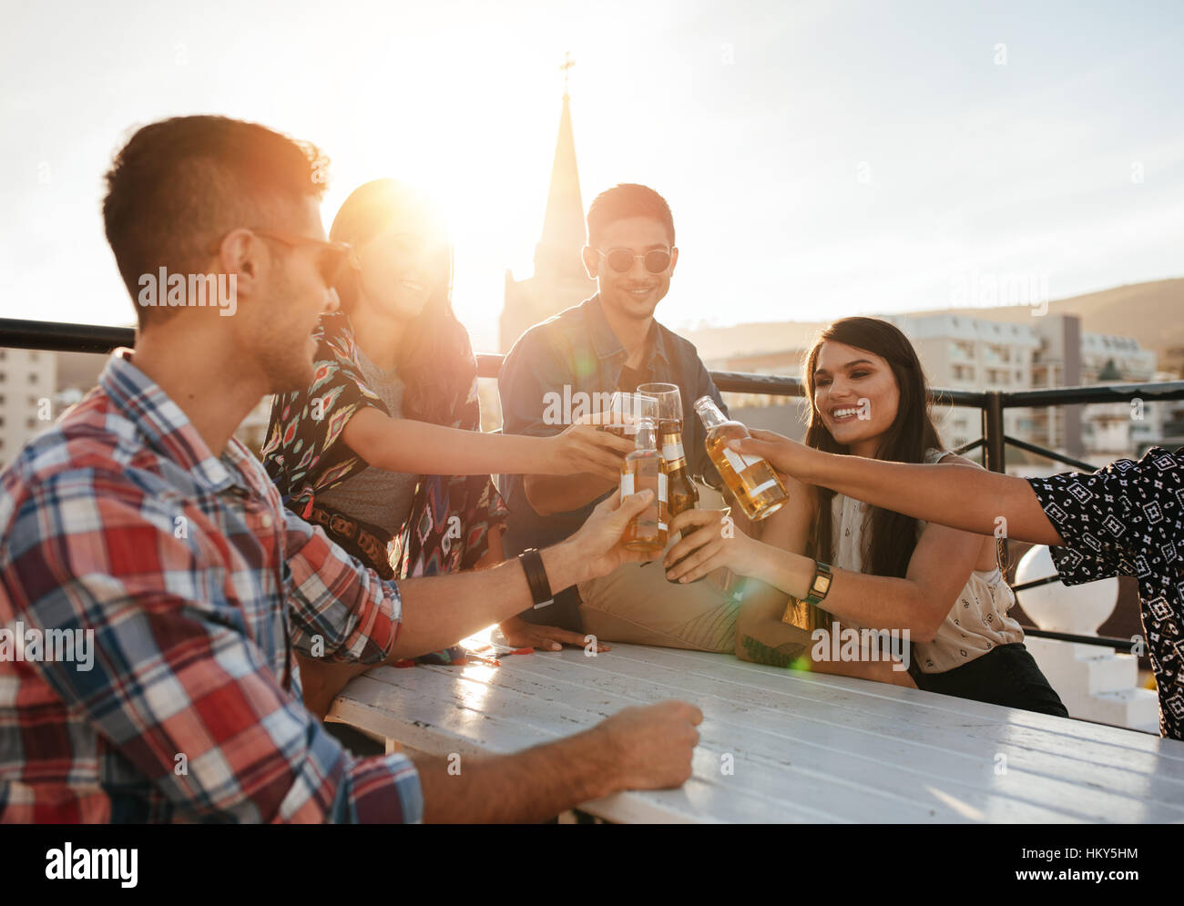 Happy young people toasting drinks at rooftop party. Young friends hanging out and enjoying with drinks. Stock Photo