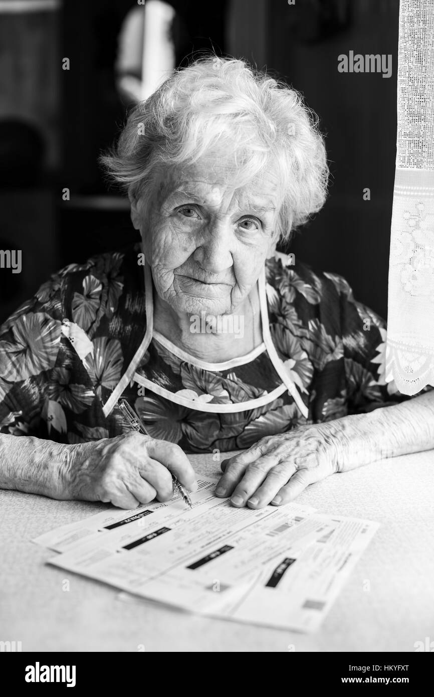 An elderly woman with a pen and receipts of utility bills. Black-and-white photo. Stock Photo