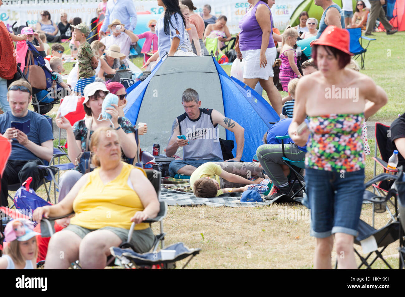 A man checking his phone while sitting in a tent surrounded by people Stock Photo