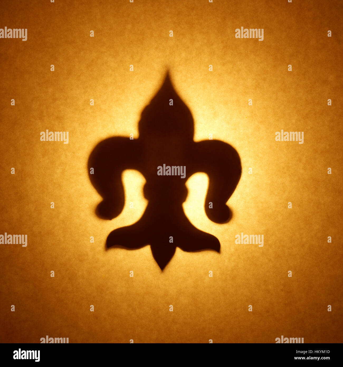 Backlit silhouette of fleur-de-lis shape cut out against brown tone paper, with spot highlight. Stock Photo