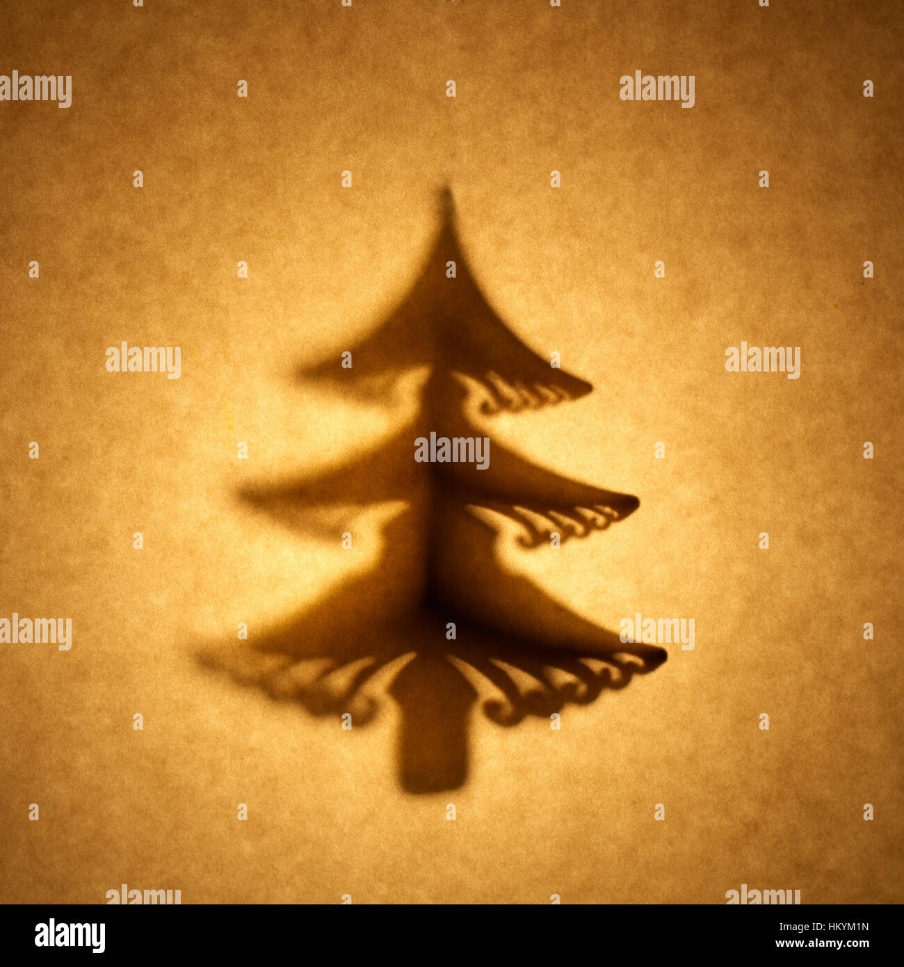 Backlit silhouette of Christmas tree shape cut out against brown tone paper, with spot highlight. Stock Photo