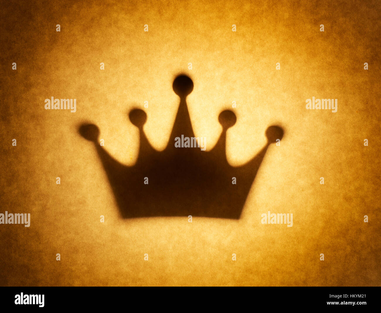 Backlit silhouette of crown shape cut out against brown tone paper, with spot highlight. Stock Photo