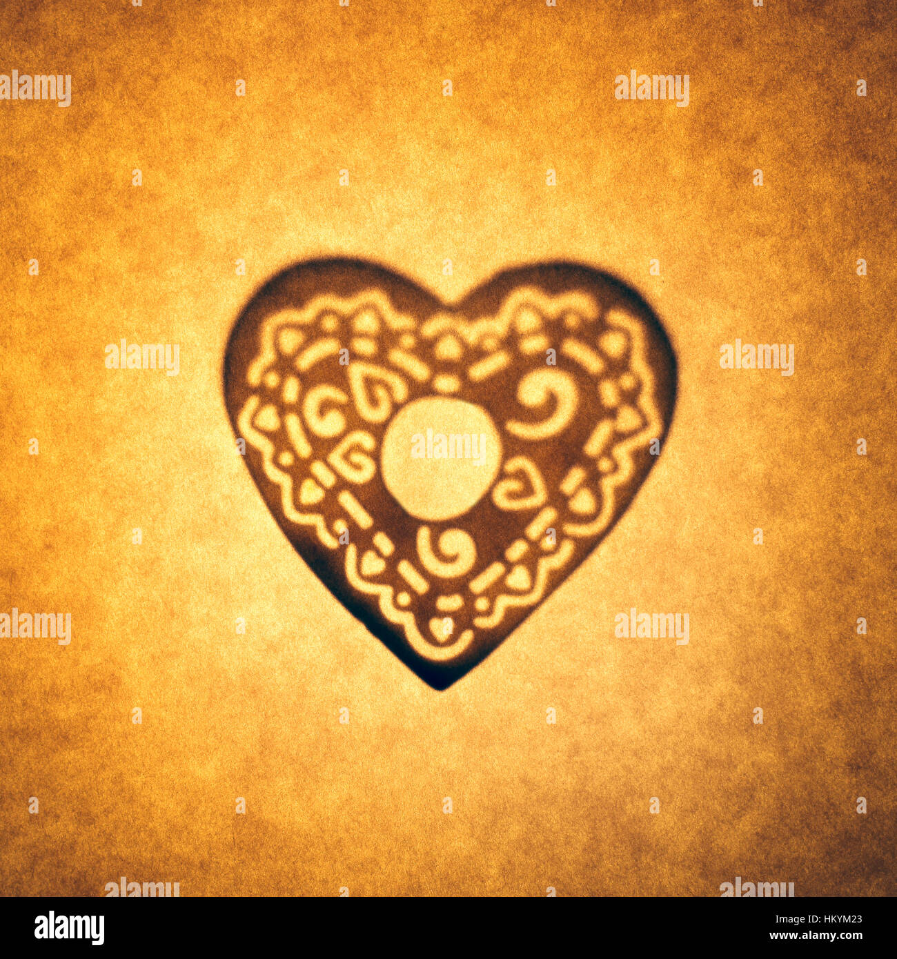 Backlit silhouette of heart shape cut out against brown tone paper, with spot highlight. Stock Photo