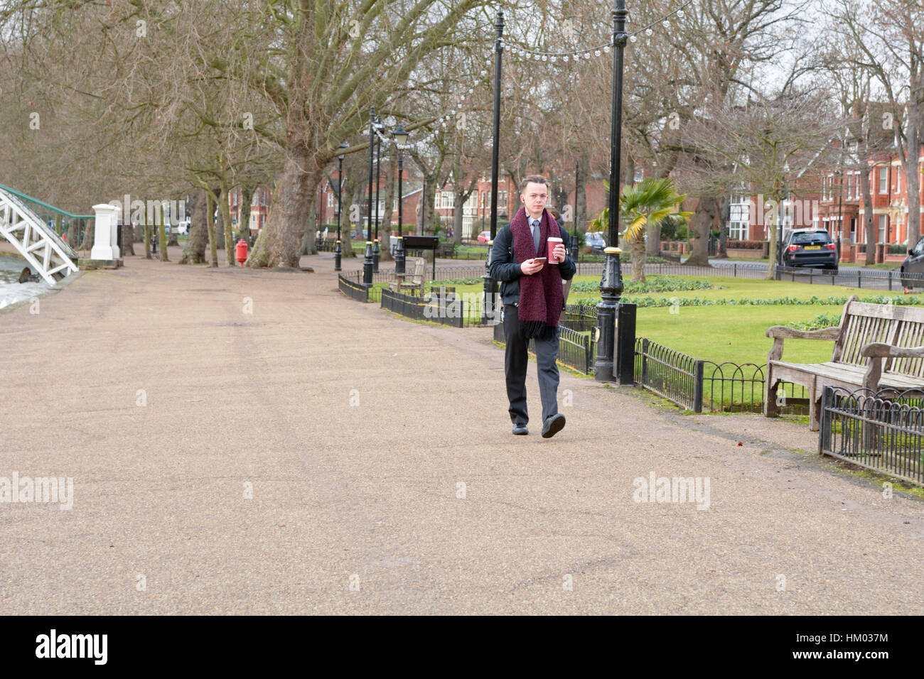 Man walking checking phone in one hand with hot drink in other in Bedford, Bedfordshire, England Stock Photo
