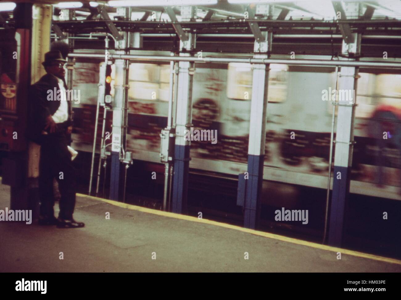 An African-American man stands on a subway station platform as a subway train car, covered in graffiti, passes by in New York City, New York, May, 1975. Image courtesy National Archives. Stock Photo