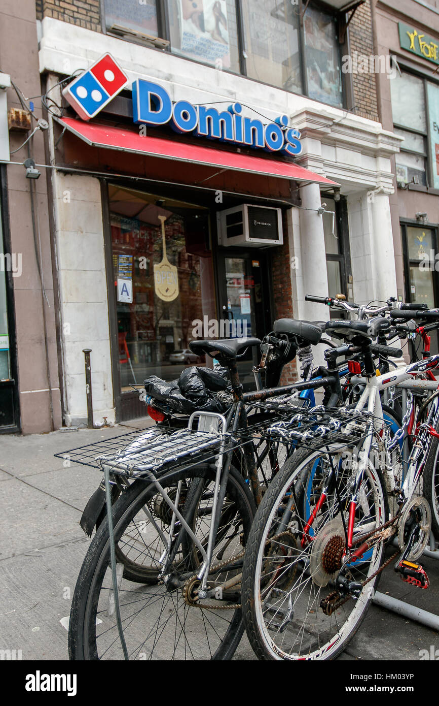 A bunch of bicycles are chained to a rack near an entrance to a local Domino's pizza store. Stock Photo