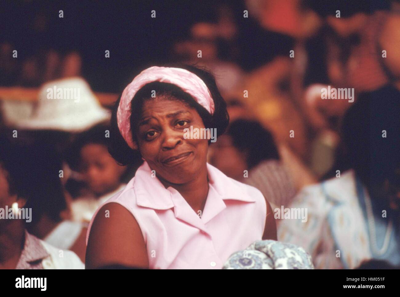 A woman with matching pink blouse and hair band raises her eyebrows and tilts her head in a large crowd outdoors in the South Side of Chicago, Illinois, 1973. Image courtesy National Archives. Stock Photo