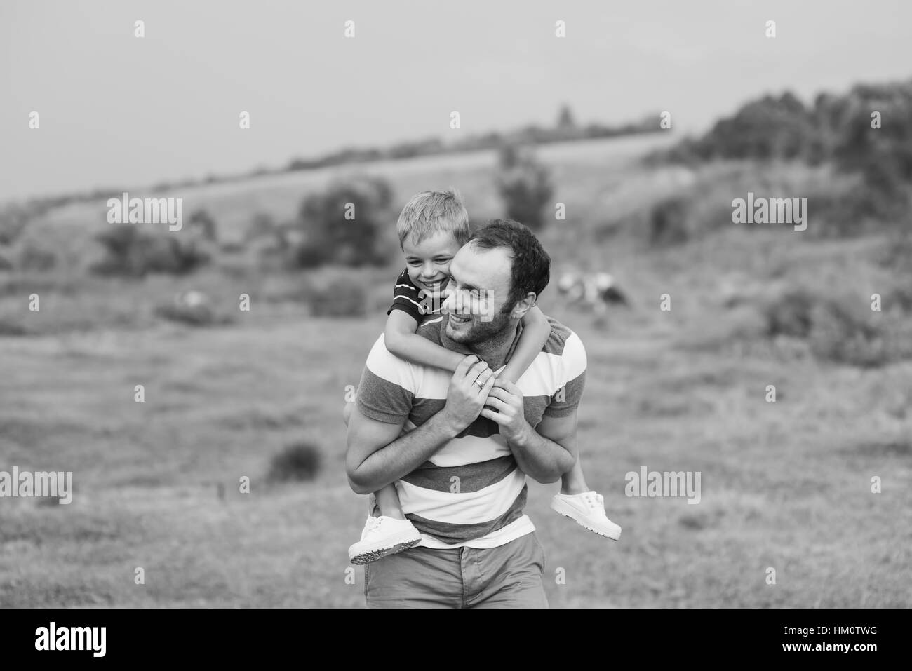 Child sitting on the shoulders of his father. Happy man with cute little baby boy. Black and white photo. Stock Photo