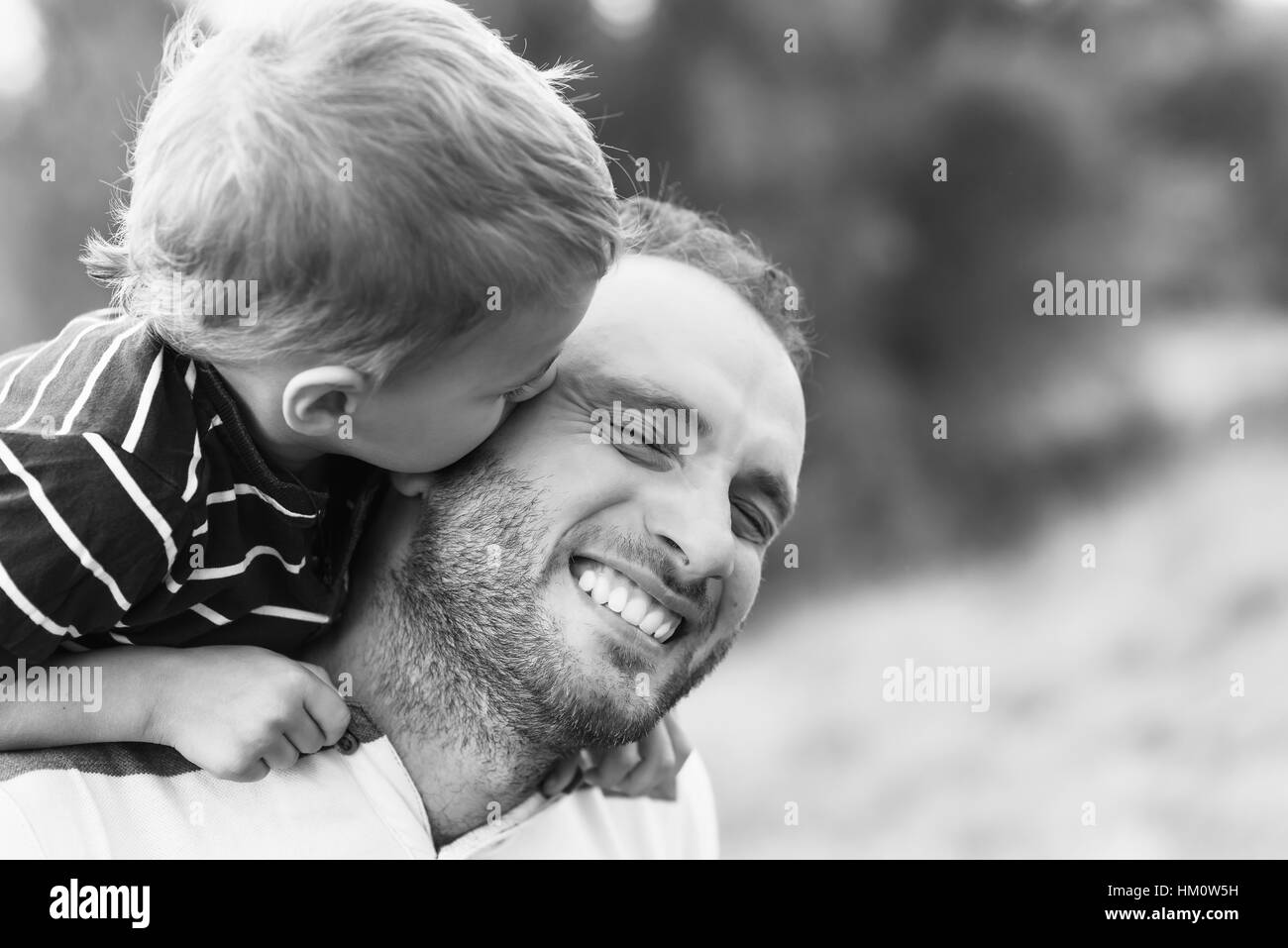 Child playing with his father. Child kissing father. Daddy playing active games with his son outside. Happy family portrait. Laughing dad with little Stock Photo
