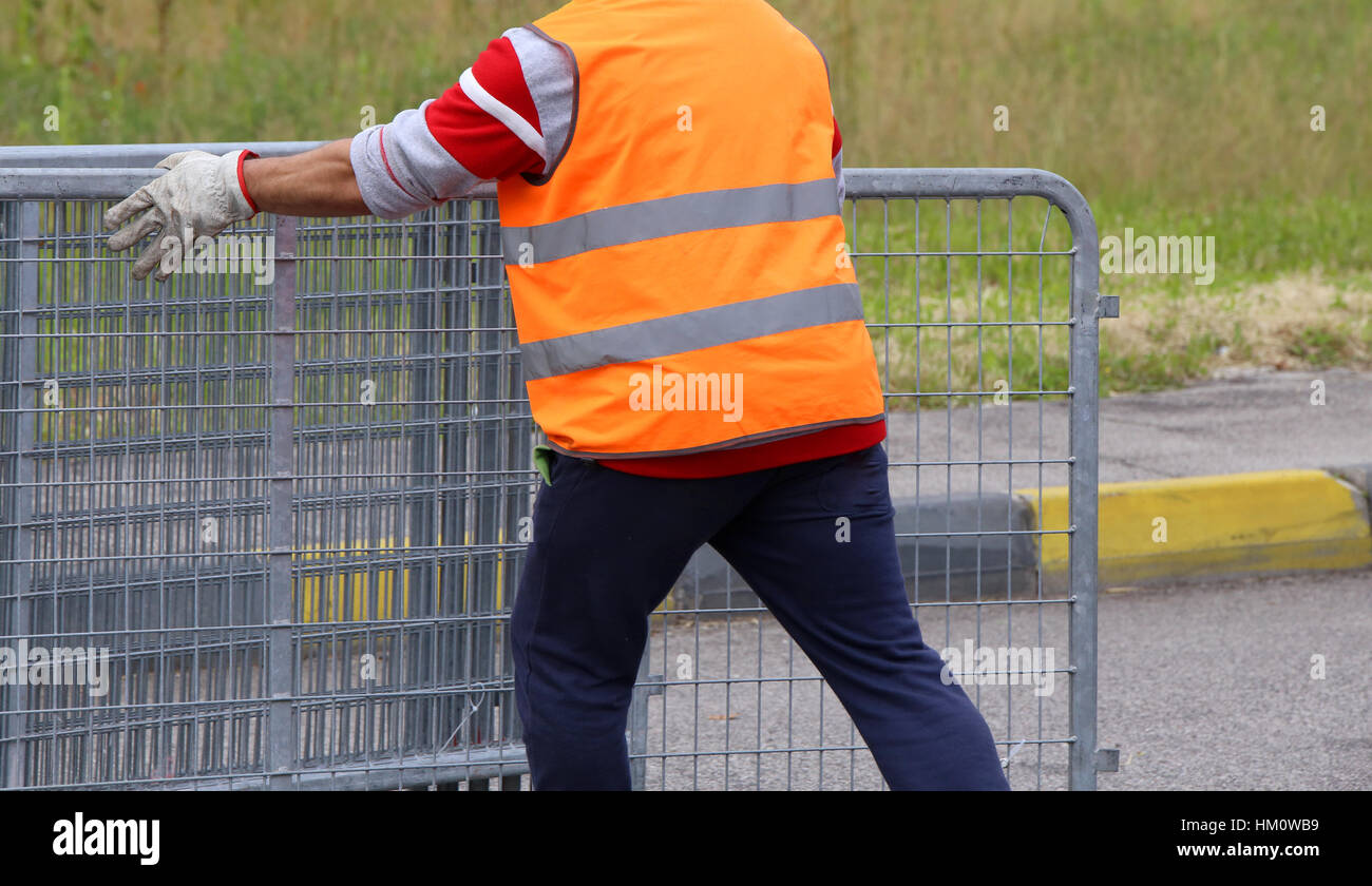 worker with orange high-visibility vest while moving the fences to delimit the space reserved for spectators Stock Photo