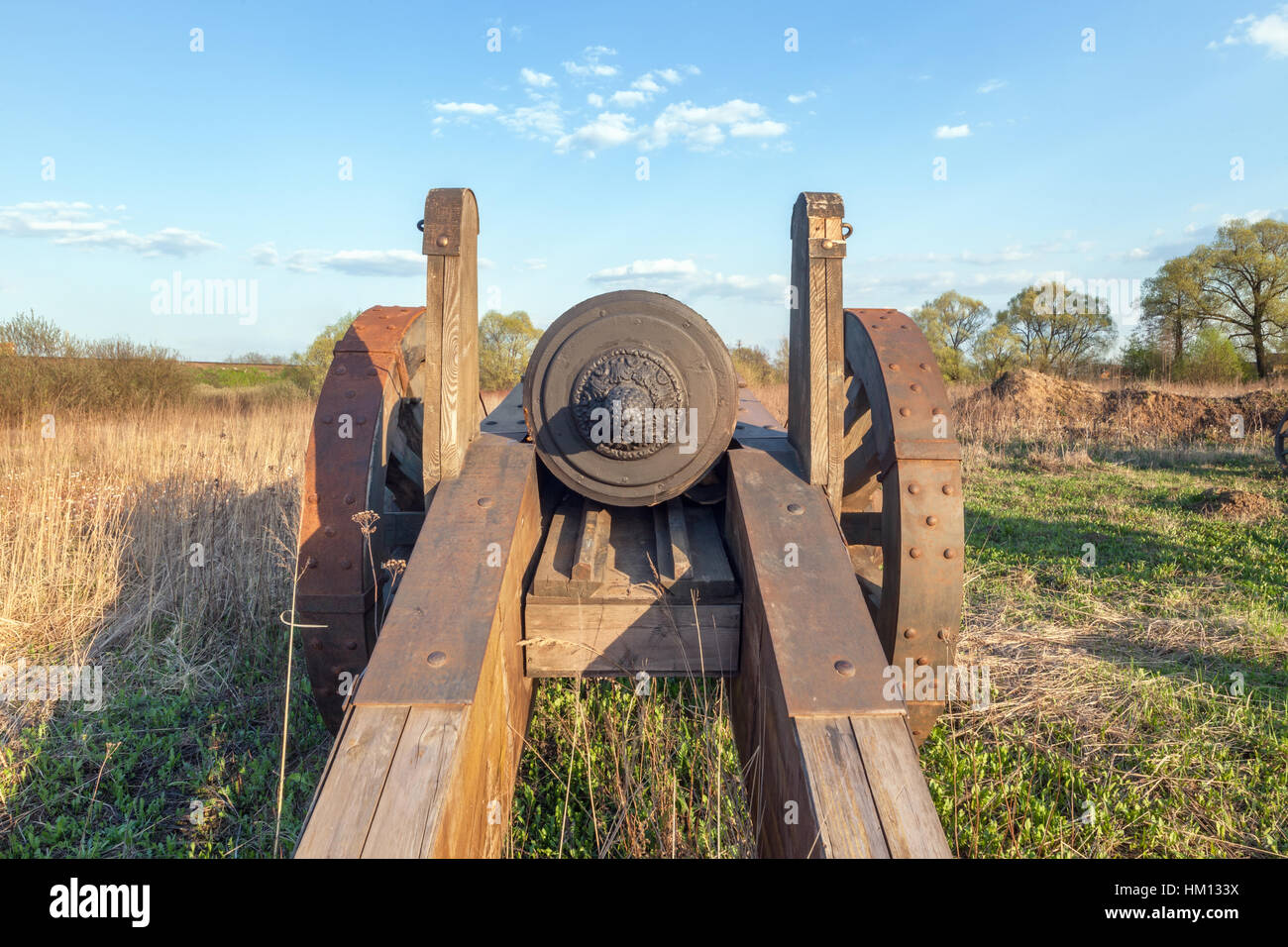 Old cannon with wooden wheels in the field on background of blue sky. Rear view Stock Photo