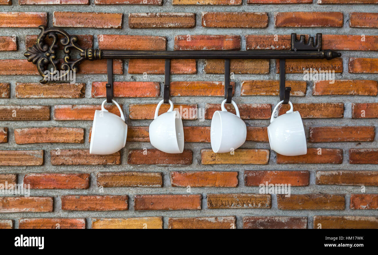 Coffee cups hanging on hooks in front of brick wall Stock Photo