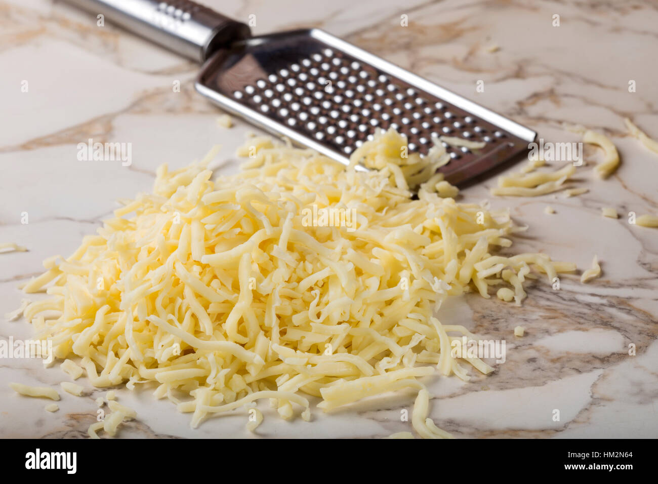 Grated mix cheese on table and one stainless steal grater in background Stock Photo