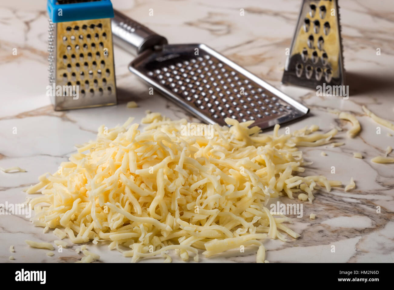 Grated mix cheese on table and three stainless steal graters in background Stock Photo