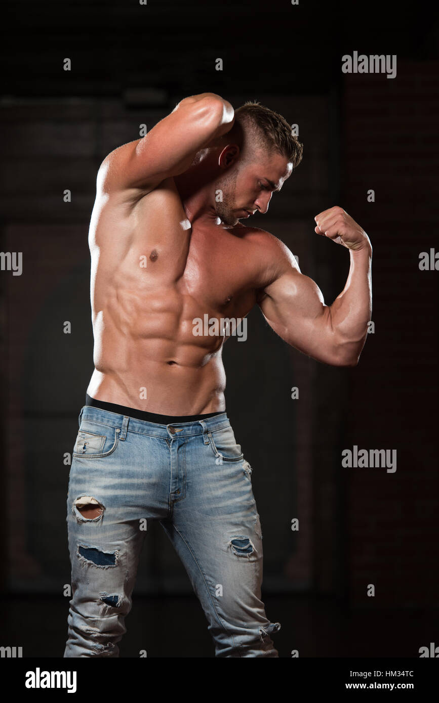 Healthy Young Man In Jeans Standing Strong In The Gym And Flexing Muscles -  Muscular Athletic Bodybuilder Fitness Model Posing After Exercises Stock  Photo - Alamy