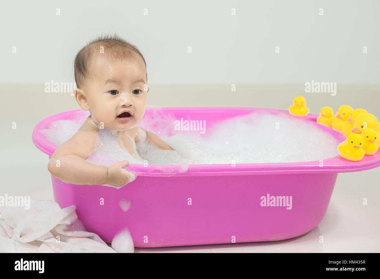 baby taking a bath in bathtub and playing with foam bubbles at home