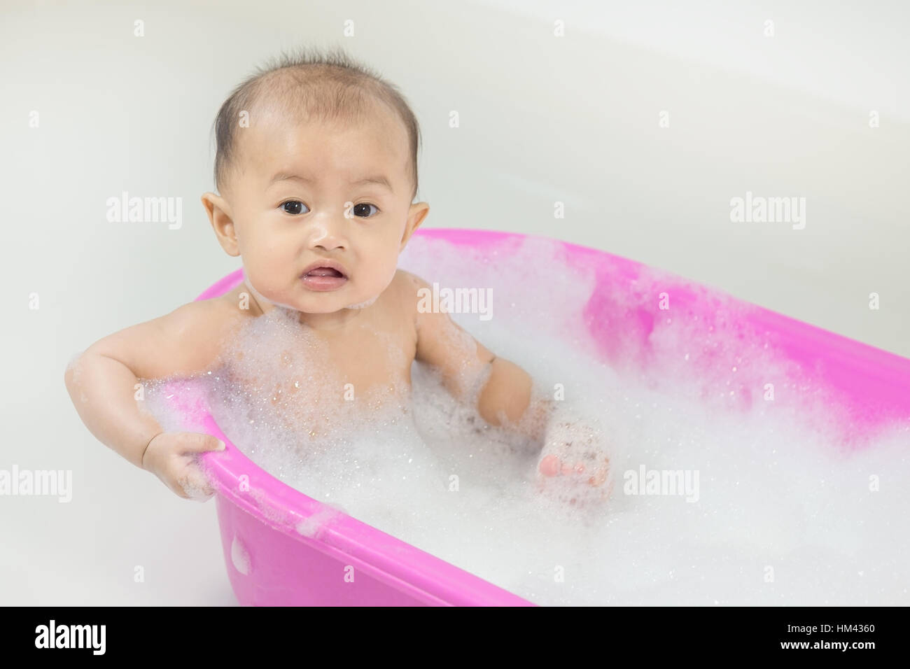 baby taking a bath in bathtub and playing with foam bubbles at home