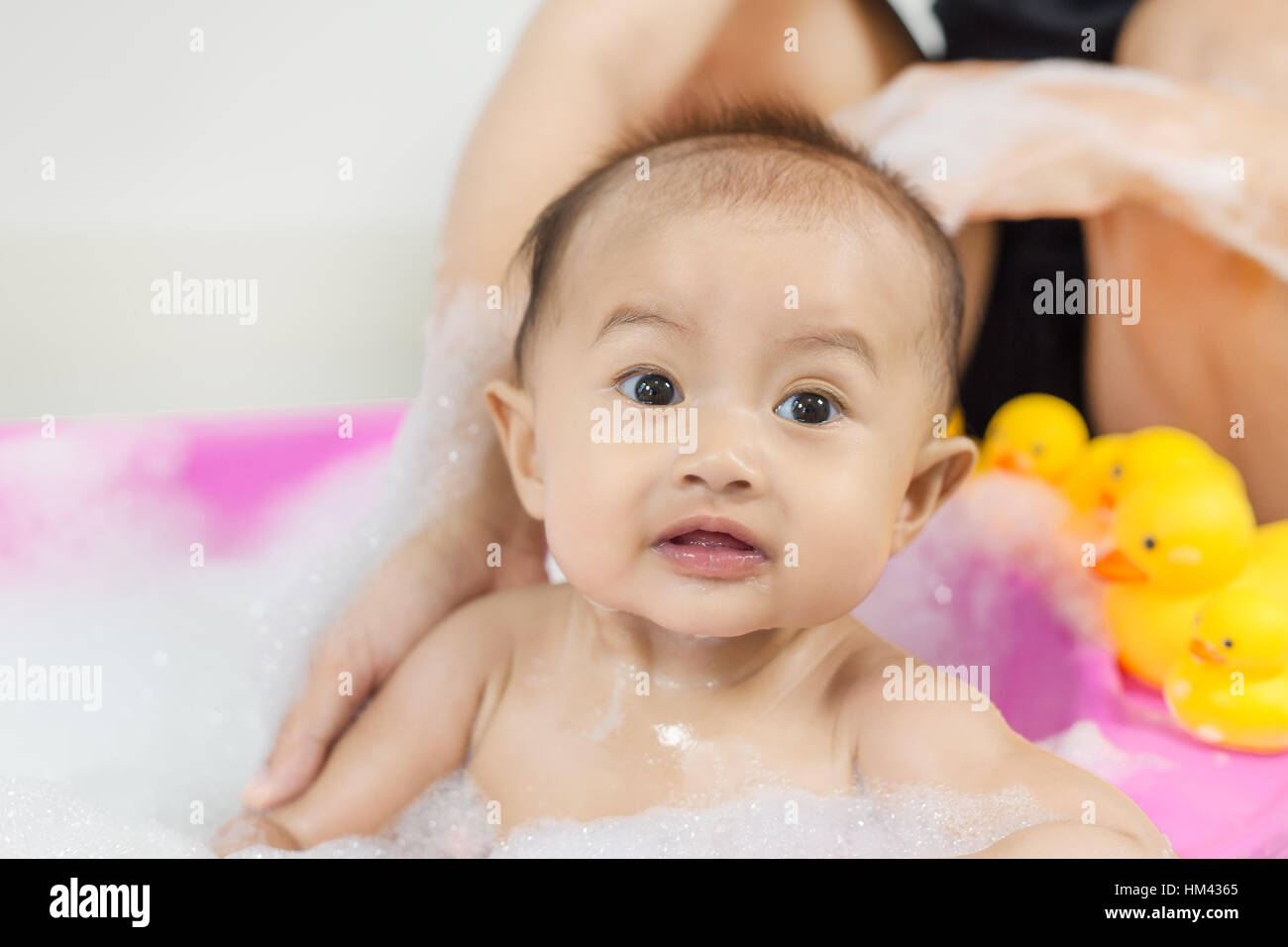 baby taking a bath in bathtub and playing with foam bubbles at home