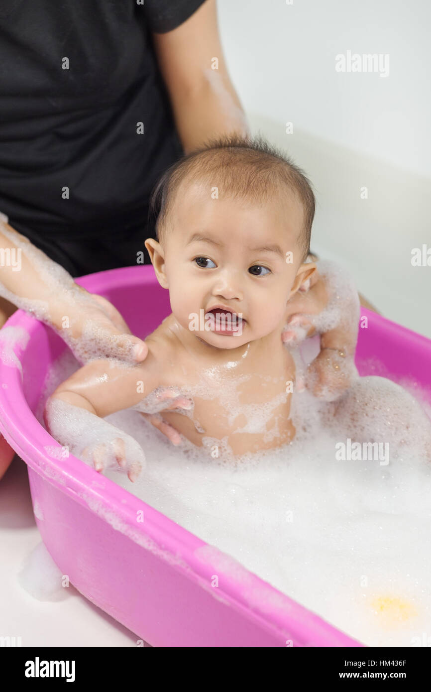 baby taking a bath in bathtub and playing with foam bubbles at home