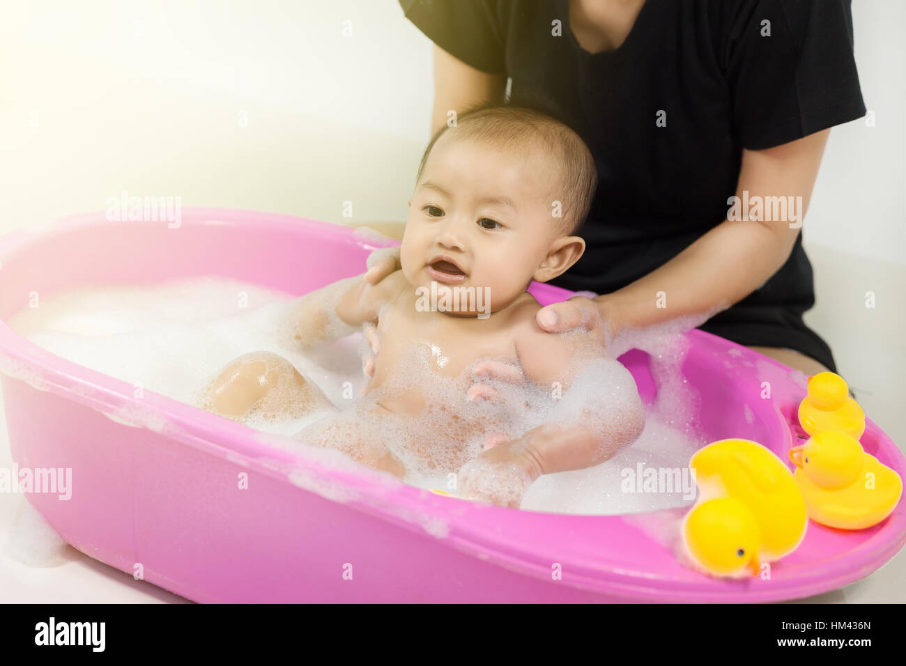 baby taking a bath in bathtub and playing with foam bubbles at home