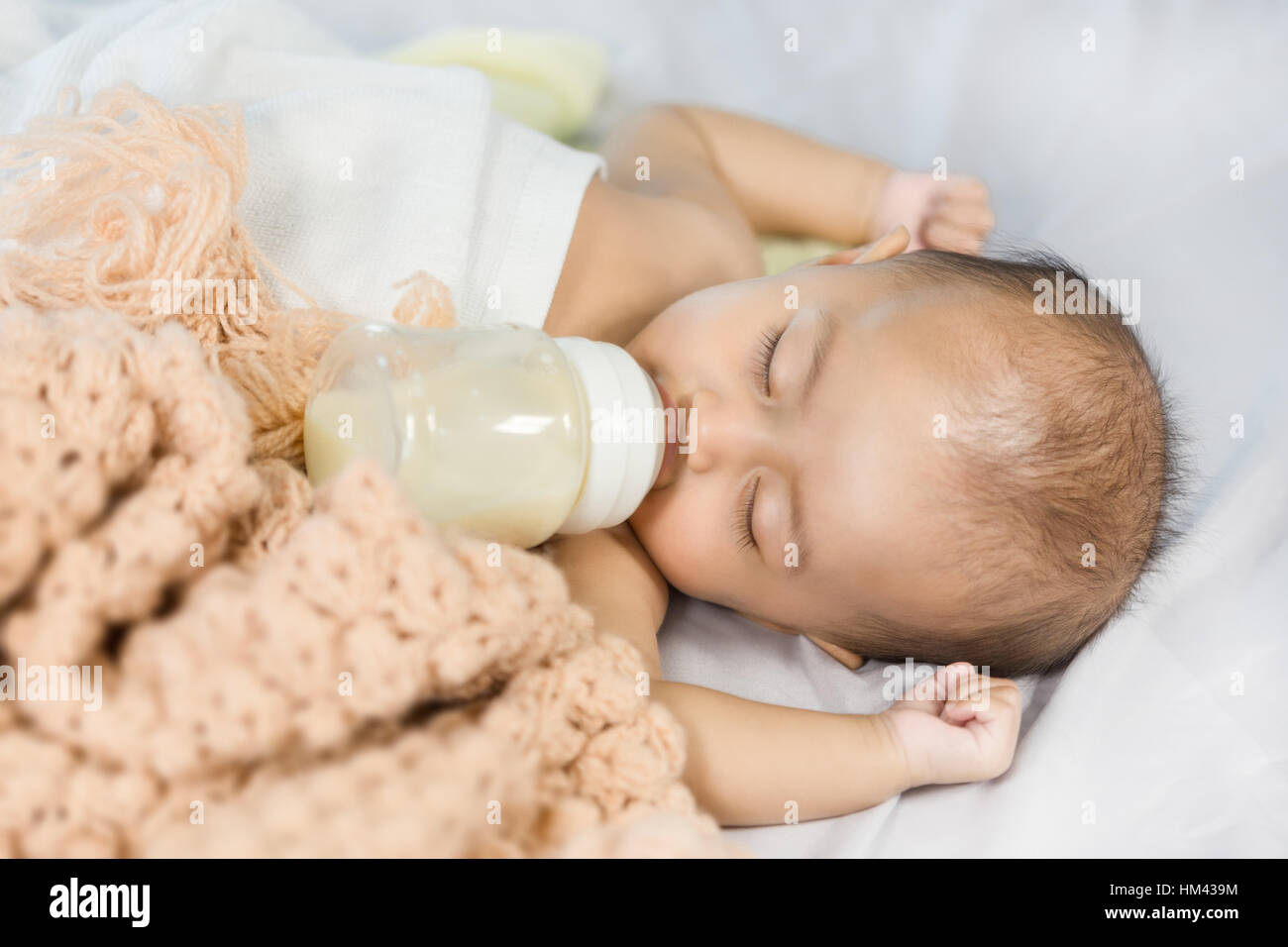 baby drinking milk from bottle and sleeping on bed at home Stock Photo