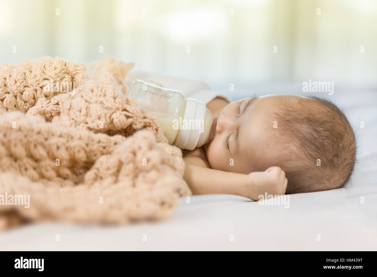 baby drinking milk from bottle and sleeping on bed at home Stock Photo