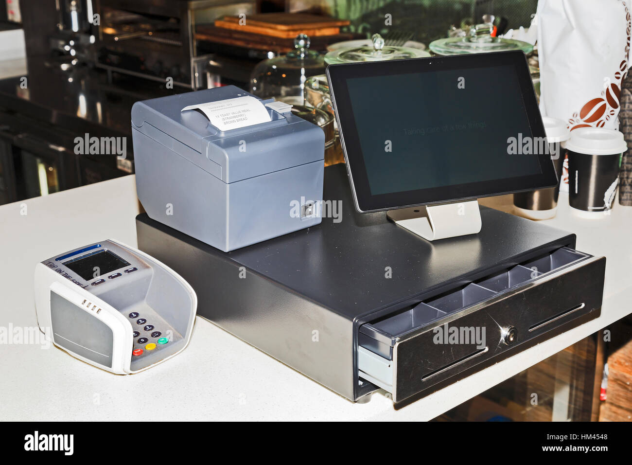 Point of sales computer terminal with touch screen tablet, cash register, mobile printer and card payment on a counter at a coffee shop. Stock Photo