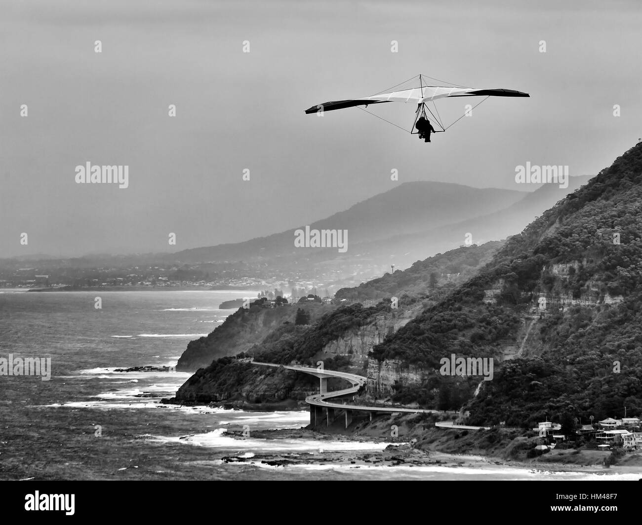Hand gliding from Stanwell tops along coastline of NSW - Grand pacific drive and Sea Cliff Bridge. Wind powered planer carries 2 adult adventurers. Stock Photo