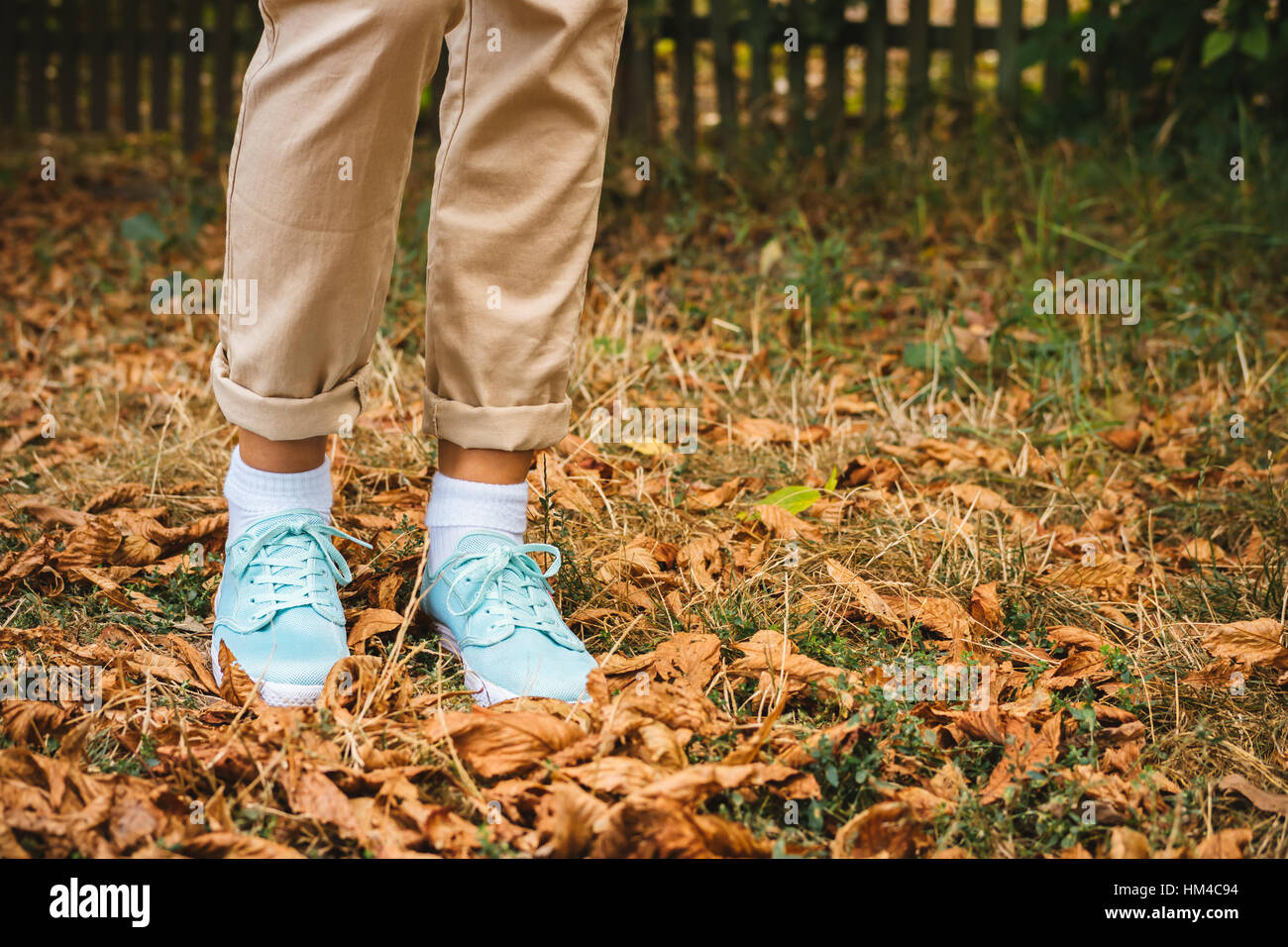 Female feet in beige pants and a turquoise sneakers are on the fallen leaves. Autumn Walk. Stock Photo