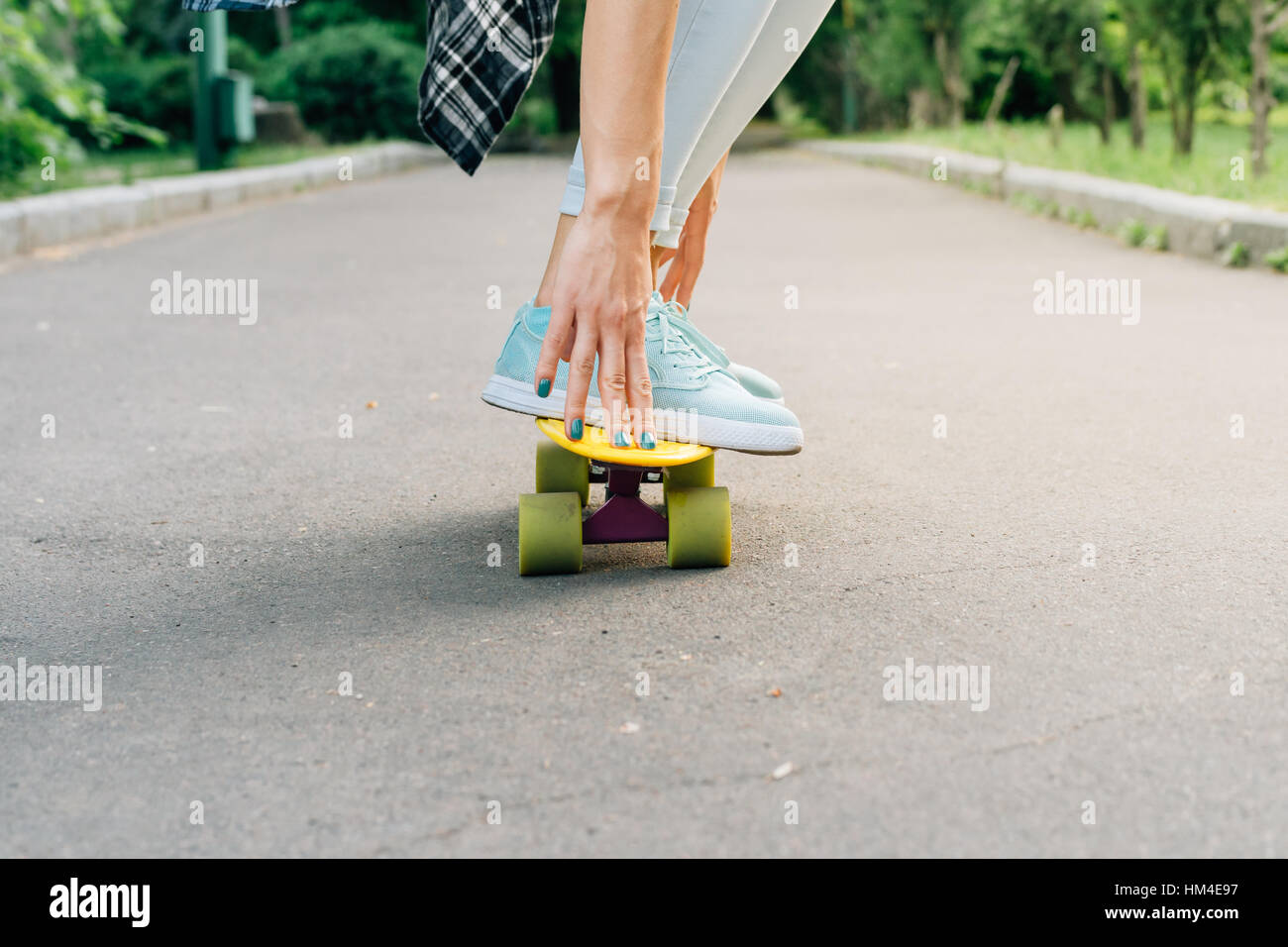 Girl rides on a skateboard on asphalt and holds balance. Active weekend in park summertime. Stock Photo
