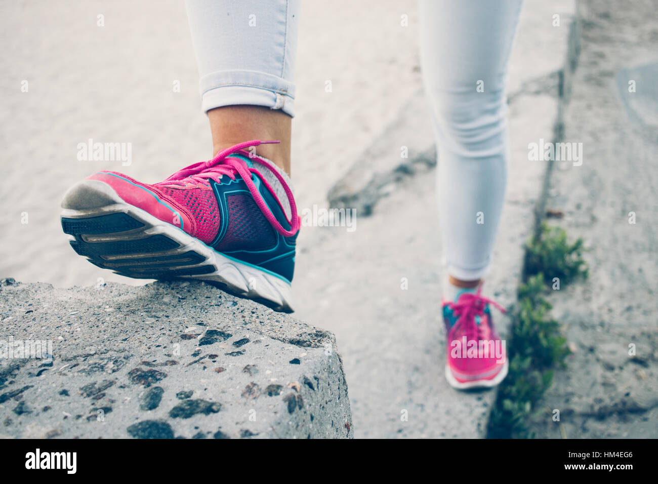 Female legs in sneakers and jeans standing on a concrete curb, toned image Stock Photo