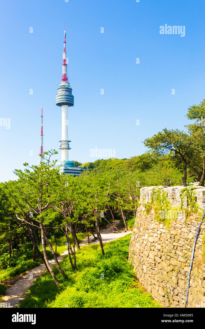 Old city wall and trees in foreground with clear view of N Seoul Tower broadcast antenna on Namsan mountain on a clear, blue sky Stock Photo